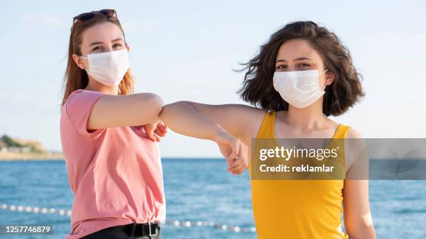 elbow bumping. a new way of greeting to avoid the spread of coronavirus (covid-19). two people women bump elbows instead of hug or handshake, beautiful girls wearing medical masks during the coronavirus covid-19 outbreak. - child saluting stock pictures, royalty-free photos & images