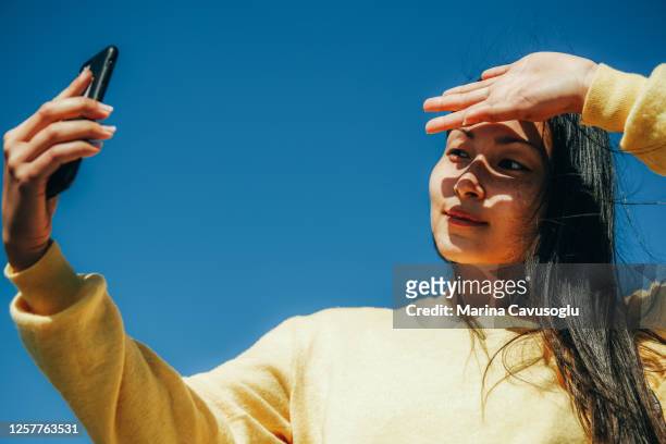 young asian girl in yellow sweater taking a selfie with her phone in a sunny day. - beautiful woman candid face 個照片及圖片檔