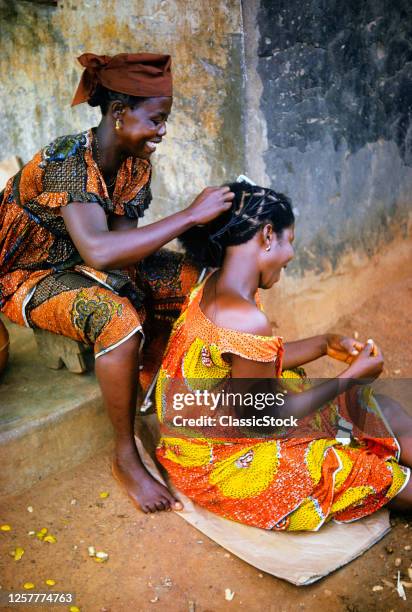 1970s Sidewalk Beauty Salon Smiling Woman Hairdresser Braiding Hair Of Client Or Friend Into A Traditional Style Ghana Africa