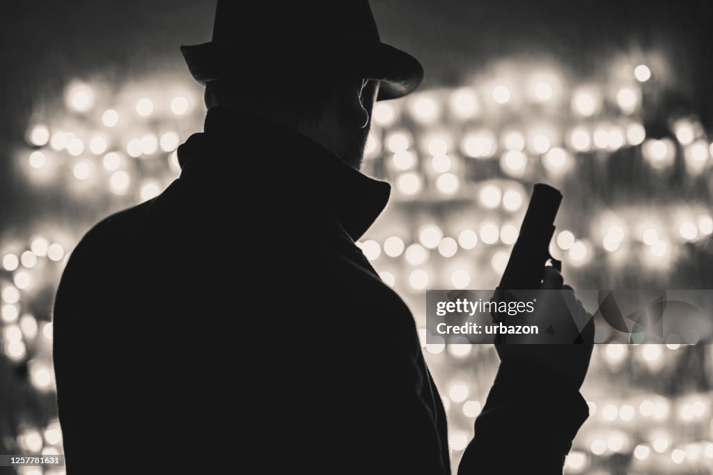 Retro-Mann in Mantel und Hut hält eine Pistole