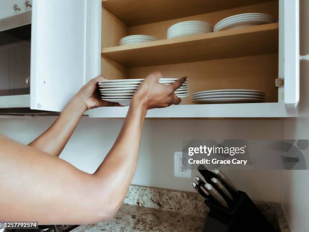 woman puts dishes into kitchen cabinet - plate set stock pictures, royalty-free photos & images