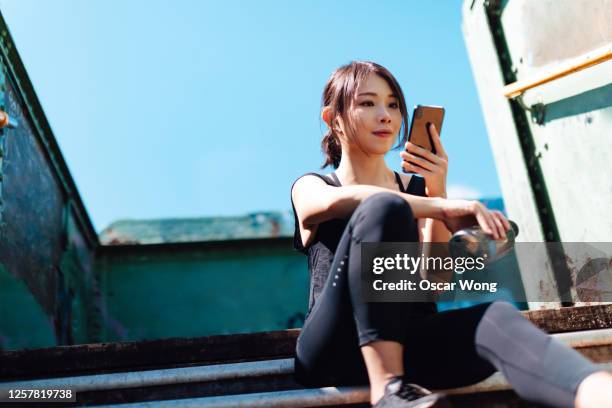 young asian female runner using smartphone while sitting on staircase to take a break in art district, city downtown - asian and indian ethnicities smartwatch phone stock pictures, royalty-free photos & images