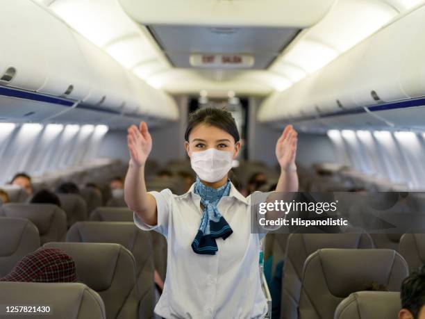 flight attendant showing the emergency exit in an airplane wearing a facemask - stewardess stock pictures, royalty-free photos & images