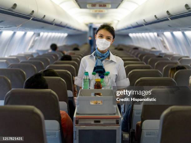 assistente di volo che serve bevande in aereo indossando una maschera facciale - airline service foto e immagini stock