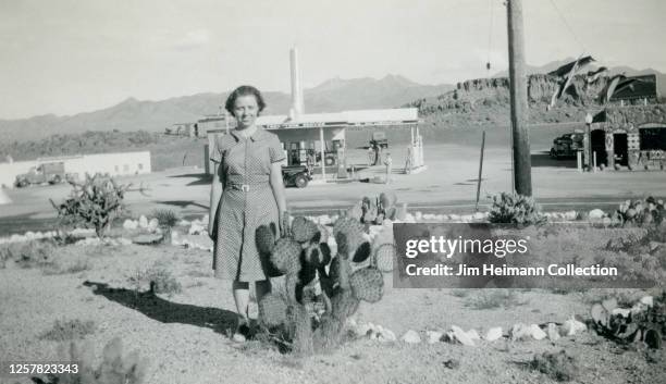 Happy girl in a dress poses with a cactus near a service station alongside Route 66 in Arizona, circa 1939.