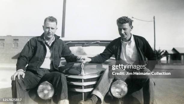 Two clean cut young men sit on the hood of a car holding hands, circa 1945.