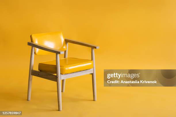 bright yellow leather and wood armchair is standing in an empty yellow background. concept of minimalism. - stuhl stock-fotos und bilder