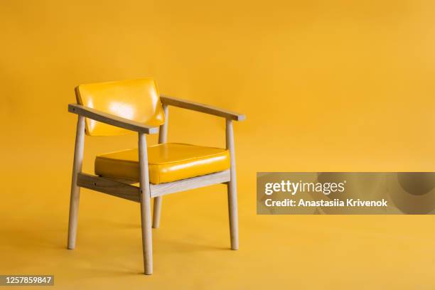 bright yellow leather and wood armchair is standing in an empty yellow background. concept of minimalism. - stoel stockfoto's en -beelden