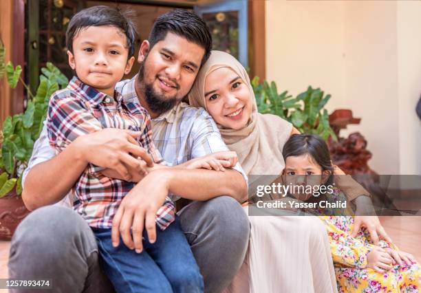 young muslim family sitting in front of their house - malay archipelago stock pictures, royalty-free photos & images