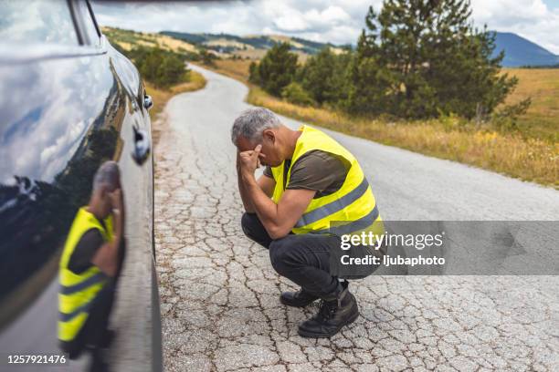 mature man kneeling next to broken car wheel - flat tyre stock pictures, royalty-free photos & images