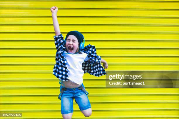 glücklicher junge mit kopfhörern tanzen und springen vor der gelben wand - siegerpose stock-fotos und bilder