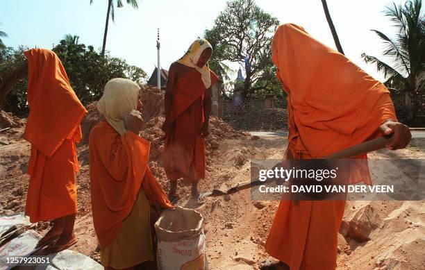 Buddhist monks, all covered up to protect them from the hot-season sun, load bags with sand 24 April to be used for the building of a bridge in the...