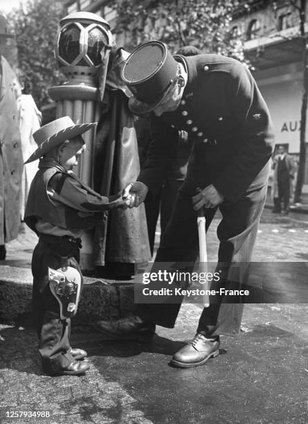 Enfant déguisé en cow-boy saluant un agent de police, le 2 juin 1948, France.