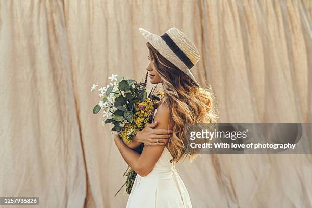 summer lifestyle outdoors photo beautiful young woman on linen backdrop in a straw hat with field flowers - kleid stock-fotos und bilder
