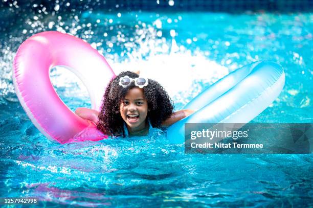 african girl splashing water with colorful inflatable ring in swimming pool. - tube girl stock-fotos und bilder
