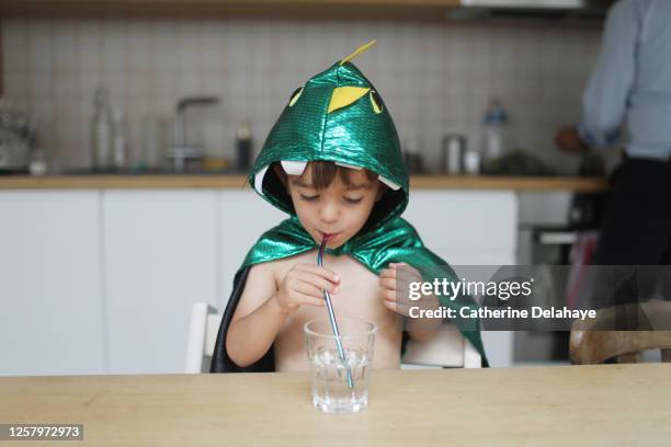 a little boy dressed as a dinosaur drinking a glass of water in the kitchen - niño-tomando-agua fotografías e imágenes de stock