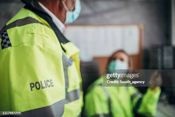 hogere mannelijke en jonge vrouwelijke politieambtenaren met beschermende gezichtsmaskers in politiebureau - verkeerspolitie stockfoto's en -beelden