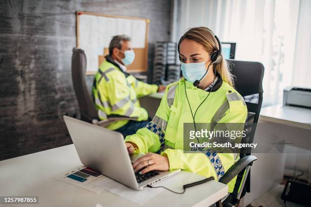 de ambtenaren van de politie met beschermend gezichtsmasker dat in bureau samenwerkt - emergency services occupation stockfoto's en -beelden
