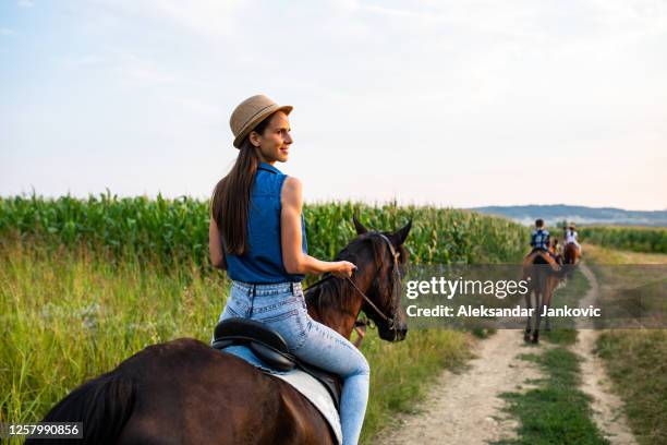 a young woman looking back smiling while stopping a horse - horse riding group stock pictures, royalty-free photos & images