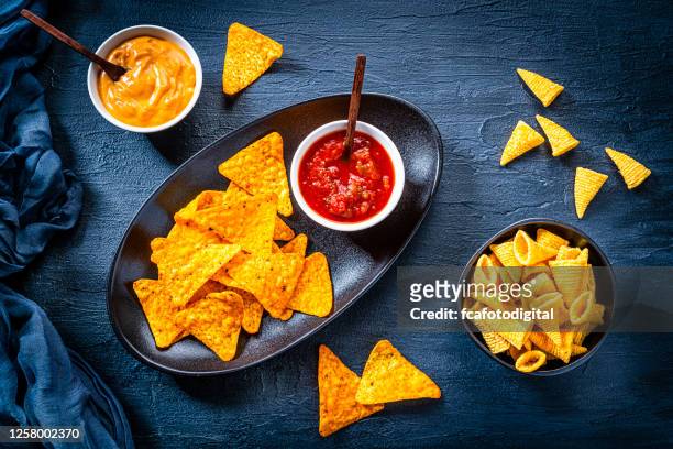 salty snack: nacho chips, corn bugles and salsa sauce shot from above on dark slate background. - bugle stock pictures, royalty-free photos & images