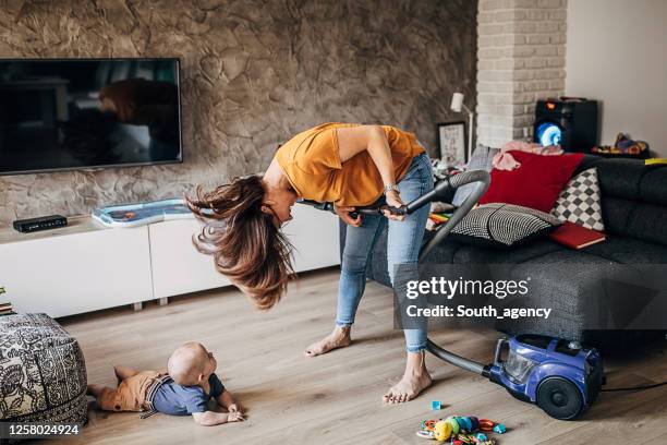 fröhliche junge mutter mit spaß mit ihrem kleinen jungen beim staubsaugen - frau tanzt im wohnzimmer stock-fotos und bilder