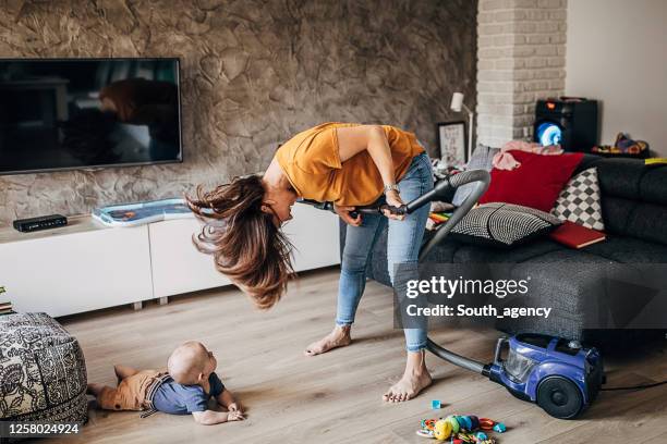 cheerful young mother having fun with her baby boy while vacuuming - spring clean and female stock pictures, royalty-free photos & images