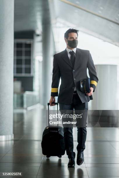 pilot walking at the airport wearing a facemask and carrying his bag - airline pilot imagens e fotografias de stock