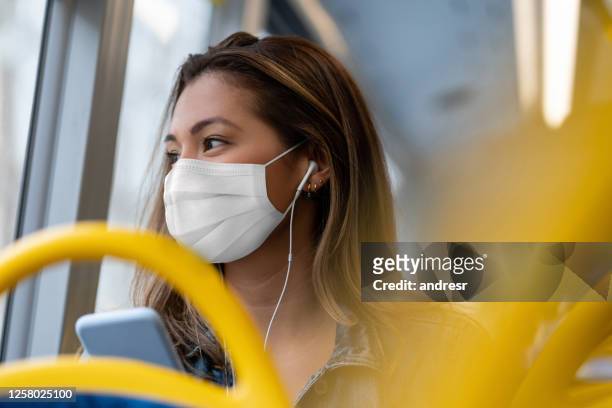 donna in sella a un autobus che indossa una maschera facciale e ascolta musica con le cuffie - autobus foto e immagini stock