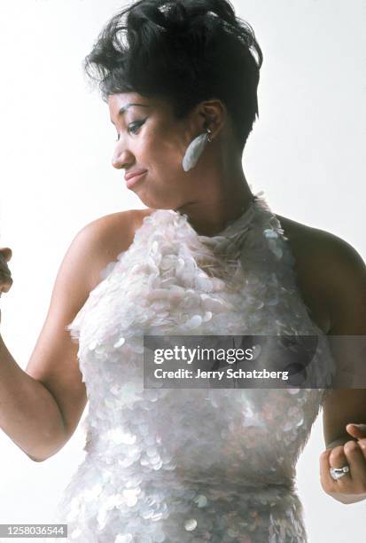 American singer Aretha Franklin , In a white iridescent plastic dress and matching earrings poses during a photo shoot for the cover of her tenth...