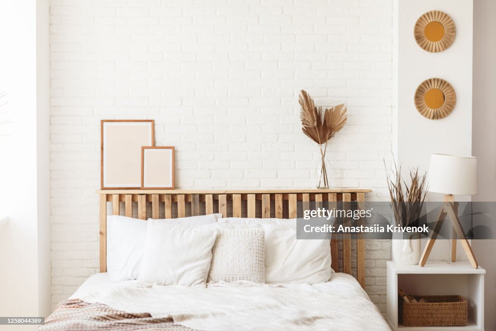 Wooden headboard with dry gold palm leaves in a glass vase and two photo frames on it. Stylish trendy decoration with copy space.