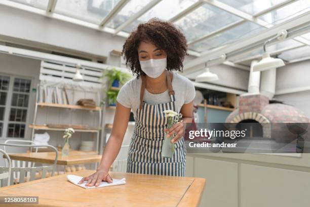 waitress at a restaurant wearing a facemask and disinfecting the tables - restaurant cleaning stock pictures, royalty-free photos & images