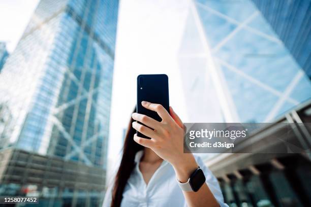 confidence and successful young asian businesswoman using smartphone on the go in financial district, against corporate skyscrapers during the day in the city - china banking regulatory commission stockfoto's en -beelden