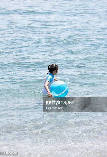 a girl holding beach ball in ocean,side view - ゴムボール ストックフォトと画像