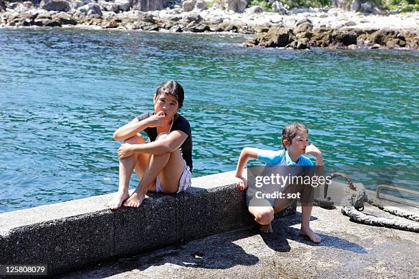 two girls sitting on the breakwater beside sea - groyne ストックフォトと画像