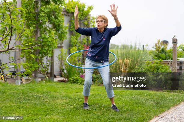 glückliche 73 jahre alte seniorin hula hooping im garten - gymnastikreifen stock-fotos und bilder