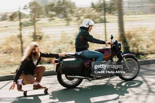side view of motorcycle towing skater - men doing quirky things stock-fotos und bilder