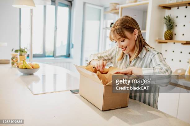 jonge vrouw pakt het pakket dat ze online besteld - packing parcel stockfoto's en -beelden