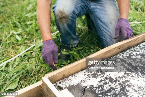 a senior man working in the backyard of a country house sawing off a wooden plank on a makeshift raft - zero effort stock pictures, royalty-free photos & images