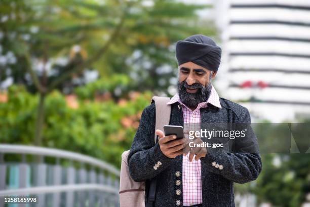 seide geschäftsmann mit turban mit smartphone - india phone professional stock-fotos und bilder