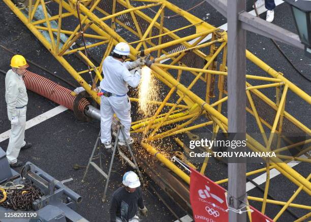 Construction worker uses a blow torch to cut off a section of a pile driver which overturned on the street at a construction site in Tokyo on April...