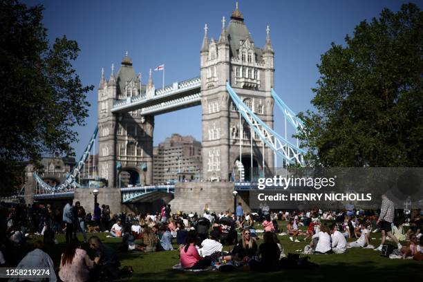 People enjoy the sunshine and the warm weather on the grass by Tower Bridge, in central London, on May 27, 2023.