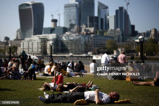 People enjoy the sunshine and the warm weather as they lay on the grass with the The Walkie-Talkie and other buildings of the City district, in...