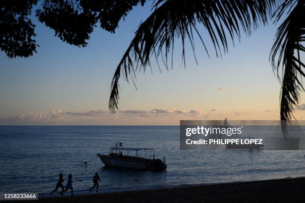 This photograph taken on late May 27, 2023 shows children running on a beach while a boat sails off the coast of French Indian Ocean island of...