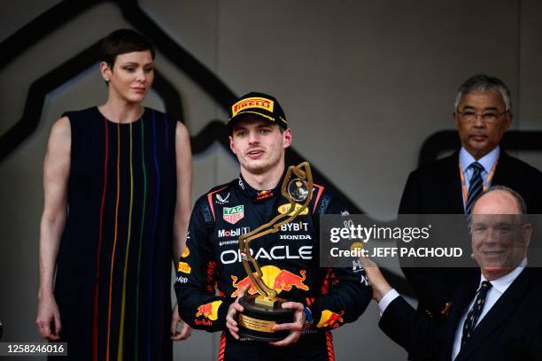 Red Bull Racing's Dutch driver Max Verstappen holds up his trophy flanked by Prince Albert II of Monaco and Princess Charlene of Monaco on the podium...