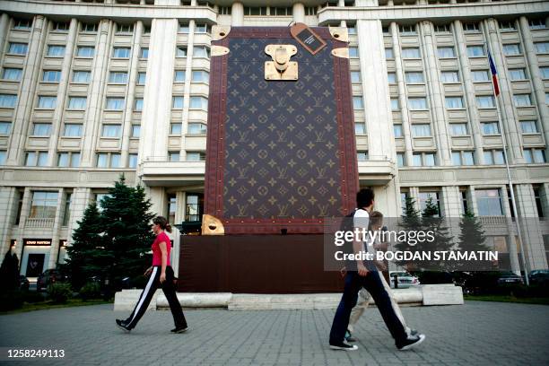 People walk on June 11, 2008 in front of a giant reproduction of a Louis Vuitton suitcase, marking the opening of a store of the French luxury...