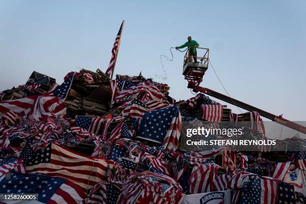 Volunteer adds fuel for the fire over US flags at the Memorial Day Watchfire in Syracuse, New York, on May 28, 2023. It is said that after a battle,...