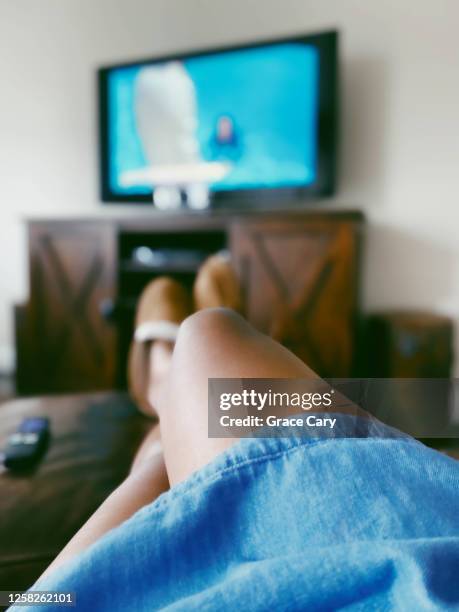 woman watches tv with feet up on ottoman - feet up tv stock pictures, royalty-free photos & images