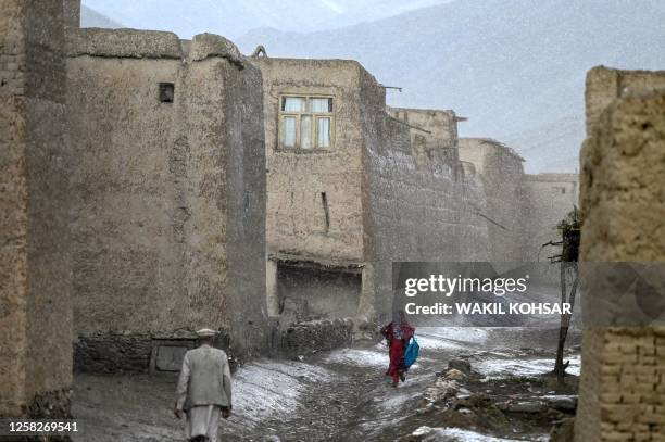 An Afghan man with a girl walk along a road amid rainfall in Tangi valley of Saydabad district in Maidan Wardak province on May 29, 2023.