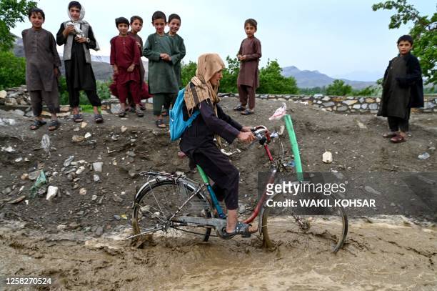 An Afghan boy rides his bicycle through rainwater along a road in Tangi valley of Saydabad district in Maidan Wardak province on May 29, 2023.