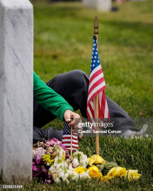 Boy sticks an American flag in the ground in front of the headstone marking the final resting place of a fallen loved one in Arlington National...